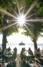 People in a beer garden under chestnut trees in Herrsching am Lake Ammer, in the background a