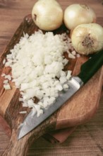 Finely chopped onion on a chopping board with a knife, wooden table, top view, no people