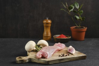 Raw rabbit tenderloin on a wooden cutting board beside fresh mushrooms and an assortment of spices.