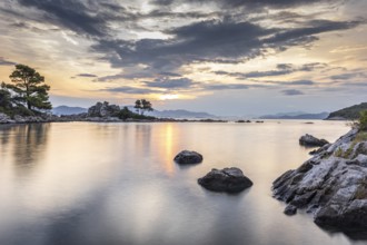 Calm sea at sunrise with reflecting clouds and rocks in the foreground, Peljesac, Croatia, Europe