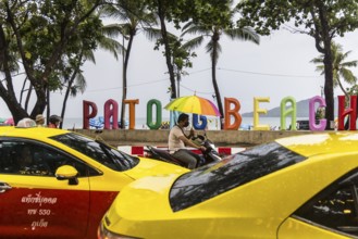 Patong Beach in rainy weather. A photo spot with coloured letters on the beach. Taxis and colourful