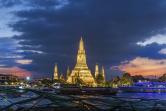 Wat Arun, Temple of Dawn at sunset with dark clouds. Boats on the Chao Phraya river. Tourist