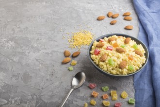 Millet porridge with candied fruits and almonds in blue ceramic bowl on a gray concrete background