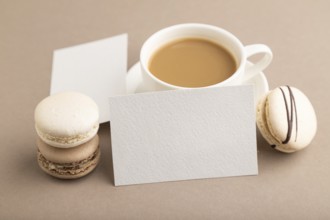 White paper business card mockup with brown and white macaroons and cup of coffee on beige pastel