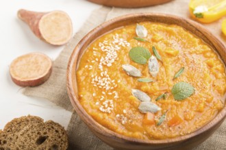 Sweet potato or batata cream soup with sesame seeds in a wooden bowl on a white wooden background