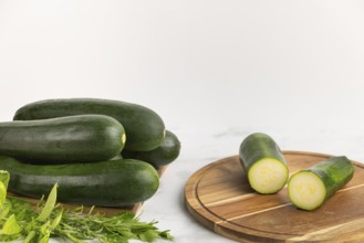 Sliced courgettes on a wooden board next to stacked whole courgettes and fresh herbs