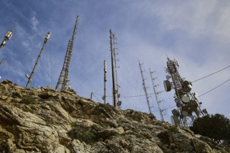 Several radio masts and antennas towering into the cloudy sky on a rocky hill, mountain top,