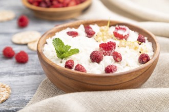 Rice flakes porridge with milk and strawberry in wooden bowl on gray wooden background and linen