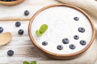 Yogurt with blueberry in wooden bowl on white wooden background and linen textile. Side view, close