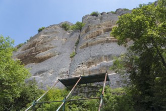 Scaffolding in front of a high rock face surrounded by trees and blue sky, rock relief, Horsemen of