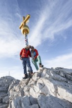 Couple, two mountaineers in front of a golden summit cross, summit of the Zugspitze, Wetterstein