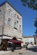 Tall stone building with characteristic windows and a flag, surrounded by trees and a clear blue