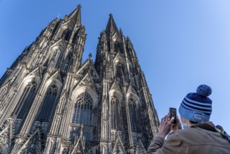 Cologne Cathedral, view of the west facade, at the north tower, tourist takes a photo with a mobile