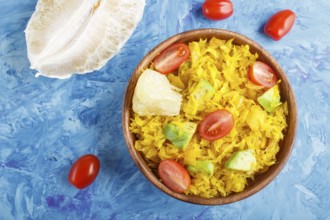 Fried pomelo with tomatoes and avocado in wooden plate on blue concrete background. Top view,