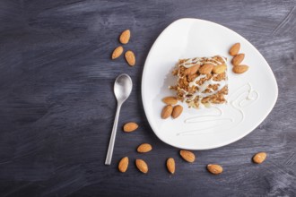 Pie with caramel, white milk sauce and almonds on a white plate on a black wooden background. top