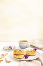 Small cheesecakes with jam and almonds with cup of coffee on a white concrete background and linen