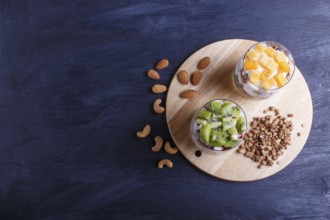 Dessert with greek yogurt, granola, almond, cashew, kiwi and persimmon on black wooden background.