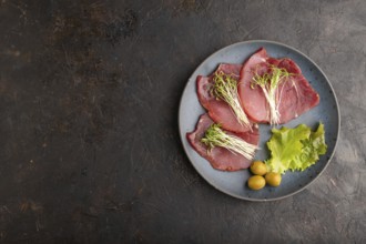 Slices of smoked salted meat with cilantro microgreen on black concrete background. Top view, flat