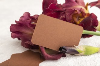 Brown business card with iris burgundy purple flowers on white concrete background. side view, copy