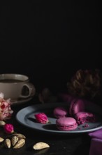 Purple macarons or macaroons cakes with cup of coffee on a black concrete background and pink