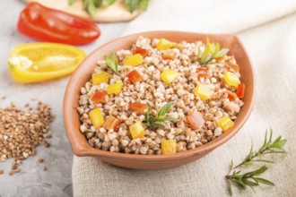 Buckwheat porridge with vegetables in clay bowl on a gray concrete background and linen textile.