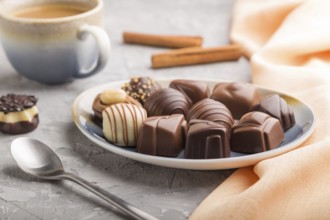 Different chocolate candies and a cup of coffee on a gray concrete background and orange textile.