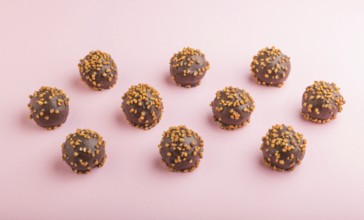 Chocolate caramel ball candies with almonds in a row on a pastel pink background. side view, close