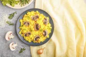 Yellow fried rice with champignons mushrooms, turmeric and oregano on blue ceramic plate on a gray