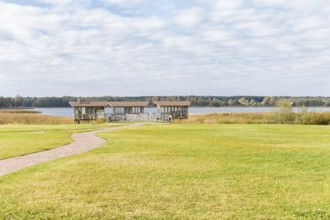 Modern gazebo near the lake with green lawn, tile path and landscape design with ornamental grasses