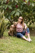 Portrait of a smiling woman and her dog, both looking at the camera, sitting on the grass