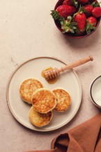 Cottage cheese pancakes with white sauce and strawberries, on a beige table, top view, selective