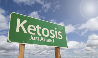 Ketosis just ahead green road sign over clouds and blue sky