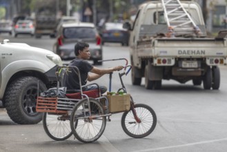 Man with an amputated leg on a hand-propelled tricycle, road traffic in Vientiane, Laos, Asia