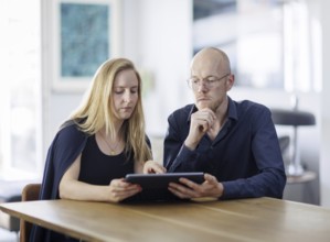 Symbolic photo. A woman and a man sit together at a table with a tablet and talk. Berlin, 13.08