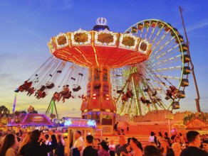 The colourfully illuminated Wellenflug chain carousel and the Ferris wheel in the evening, Cranger