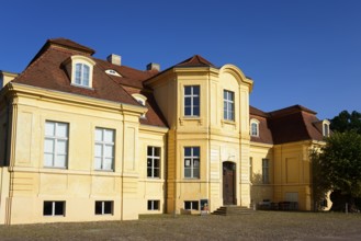 A sunlit baroque building painted yellow under a clear blue sky, Reckahn Castle, manor house, manor