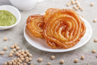 Traditional indian candy jalebi in white plate with mint chutney on a gray concrete background.