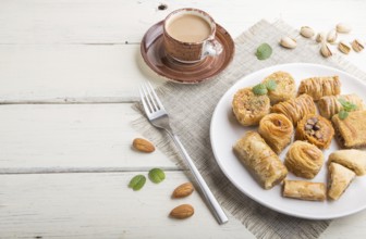 Traditional arabic sweets (kunafa, baklava) and a cup of coffee on a white wooden background and