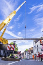 A yellow lifting crane on a busy construction site under a blue sky with buildings in the