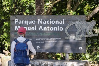 Tourist standing in front of sign at the entrance of the national park, Manuel Antonio National