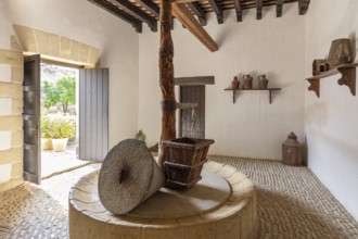 Rustic interior with antique olive oil press and wooden beams, surrounded by pots, Jerez