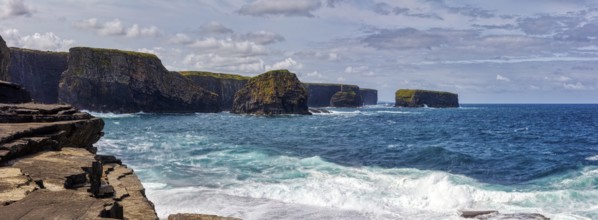 Dramatic scenery of cliffs with crashing waves and vast sea under a cloudy sky, Kilkee