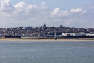 Coastal view with a strip of beach and urban background with prominent tower in clear sky,