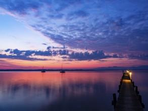 Sailing boats and jetty on Lake Chiemsee at dawn, with the Chiemgau Alps in the background,