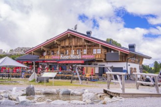 A rustic Alpine restaurant with wooden beams and outdoor seating against a mountain backdrop,