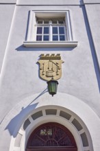 Facade of a whitewashed house in the classicist style with the coat of arms of the salt boiling