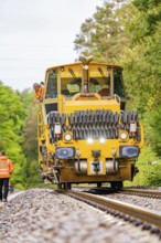 Front view of a yellow ballast compactor, worker on rails, track construction Hermann Hesse