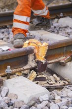 Close-up of a damaged section of track with a construction worker dressed in orange in the