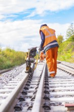 A worker with a machine on the railway tracks, working in the open air, rail welding, track