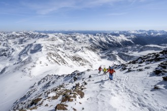 Ski tourer on foot, carrying skis on backpack, mountain panorama, snow-covered mountain landscape